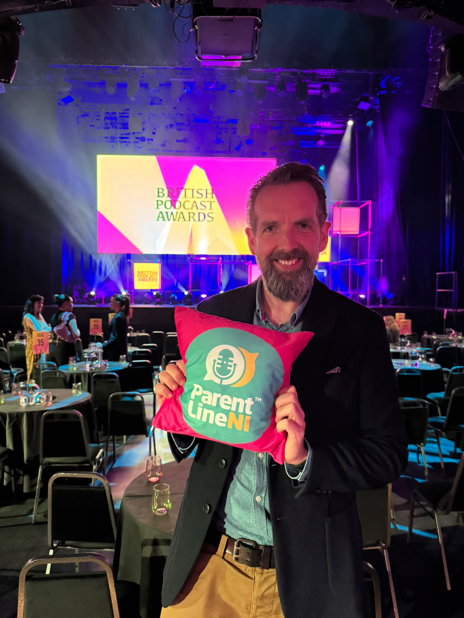Roger Gowdy producer of the Parentline Podcast pictured in the main hall at the awards. He is holding a cushion with the Parentline Podcast branding that are given out to all podcasts who are shortlisted.