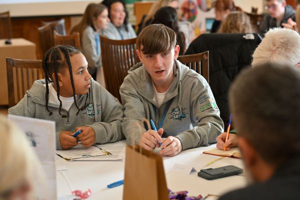 This photo shows two of the young people from Be Cyber Safe NI sitting at the table having a group discussion as part of the Cyber Cafe event. 