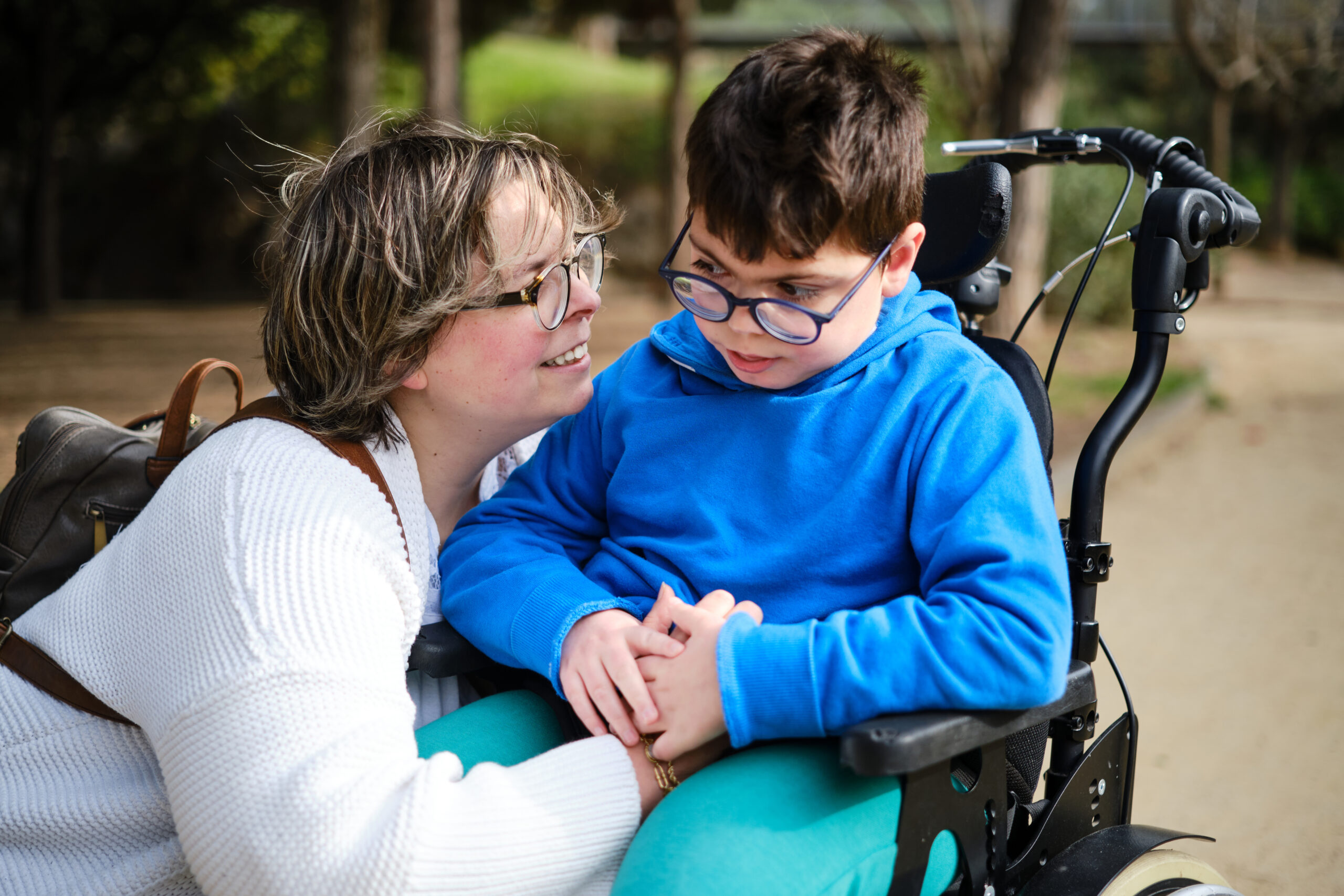 Boy in wheelchair outdoors with woman who is smiling at him